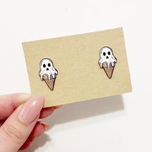 May include: Two white ghost ice cream cone enamel pins on a brown card. The ghost ice cream is melting and has a black skull face.