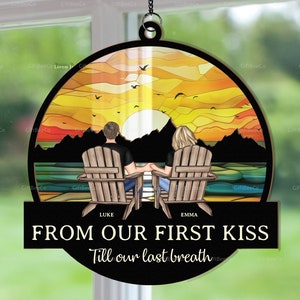 May include: A round wooden sign with a sunset scene, two figures in Adirondack chairs, and the text "FROM OUR FIRST KISS Till our last breath." The sign is suspended by a chain and features the names "LUKE" and "EMMA".