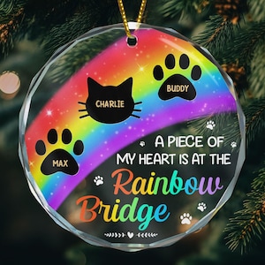 May include: A clear, faceted ornament with a rainbow design and the text "A Piece of My Heart is at the Rainbow Bridge." Features paw prints, a cat silhouette, and the names "Charlie," "Buddy," and "Max."