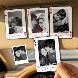 May include: A collection of playing card-shaped car visor clips featuring black and white photos of couples. Each card has a red suit symbol and romantic text. One card is held by a hand.