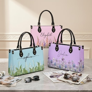 May include: Three pastel-coloured tote bags, light blue, pink, and lavender, each with a floral design and a name: Sophia, Elizabeth, and Julia. The bags have black handles and hardware. Sunglasses and magazines are in the foreground.