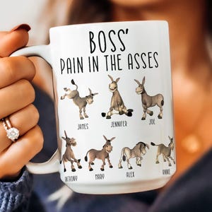 May include: White ceramic mug with the text "Boss' Pain in the Asses" and cartoon donkeys with names printed below each donkey. The names are: James, Jennifer, Joe, Anthony, Mary, Alex, and Annie.