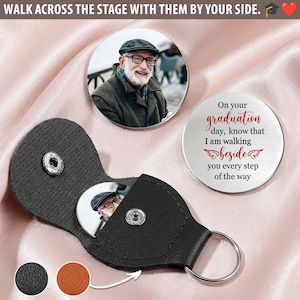 May include: A black leather keychain with a silver snap closure, holding a round photo. Two round metal keepsakes are visible, one with a photo and the other with the text "On your graduation day..." The text "WALK ACROSS THE STAGE WITH THEM BY YOUR SIDE" is at the top.