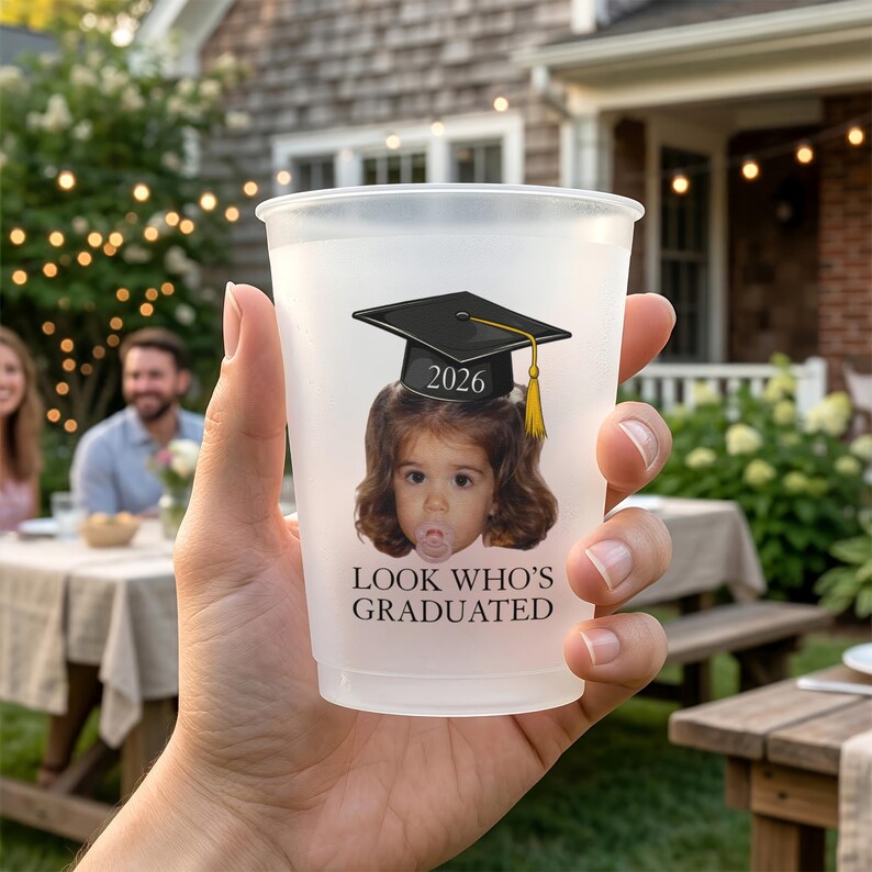 Pu&ograve; includere: Un bicchiere di plastica smerigliata con un design a tema laurea. Il bicchiere presenta una grafica di un bambino con un cappello di laurea con l'anno 2026 e il testo "LOOK WHO'S GRADUATED".