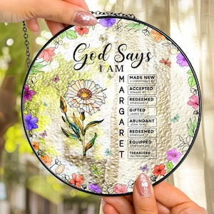 May include: A round, stained-glass window art piece with a floral and butterfly design. The text "God Says I AM" is displayed, along with a list of affirmations. The piece is held by a person.
