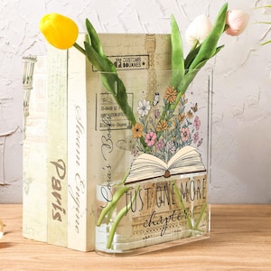 May include: A clear acrylic vase with the text "JUST ONE MORE chapter" and a floral design. The vase holds yellow and pink tulips. Behind the vase are two books with the words "Paris" and "Steam Engine".
