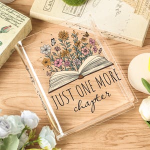 May include: Clear book cover with floral and butterfly design. The cover features an open book illustration with flowers and butterflies, and the text "JUST ONE MORE chapter".