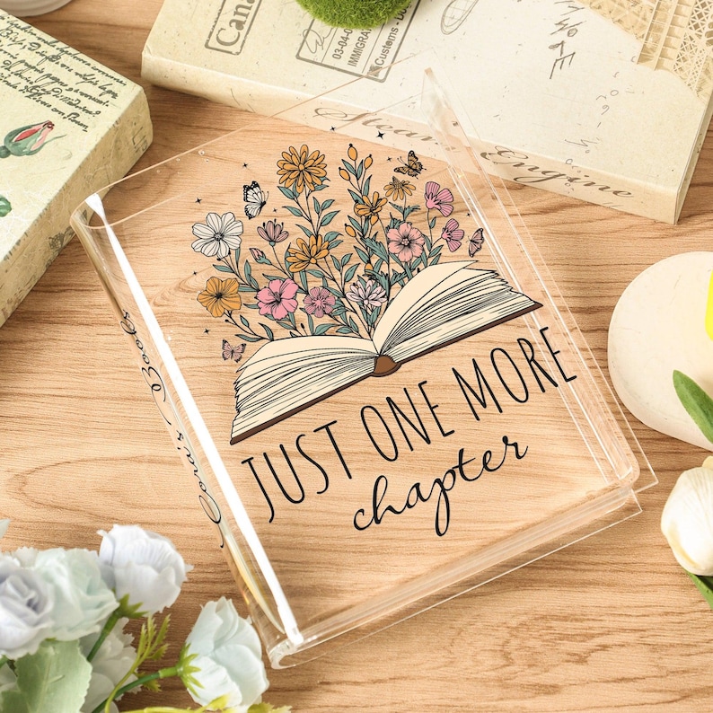 May include: Clear book cover with floral and butterfly design. The cover features an open book illustration with flowers and butterflies, and the text "JUST ONE MORE chapter".