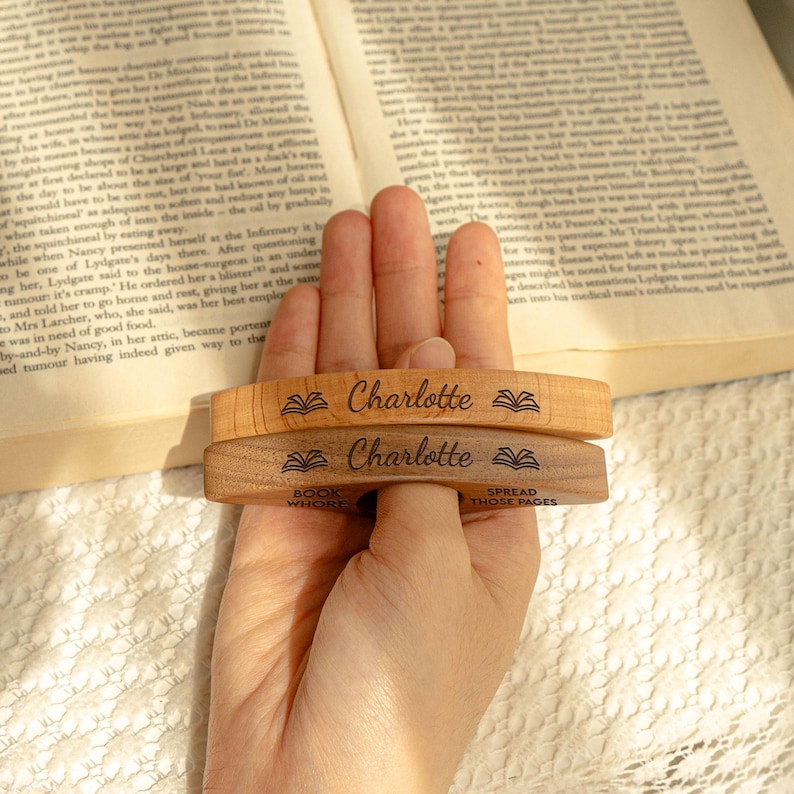 May include: Two wooden bookmarks with the name "Charlotte" engraved on them, along with a book icon. One bookmark is light-colored, the other is dark. The bottom bookmark has the phrases "BOOK WHORE" and "SPREAD THOSE PAGES".