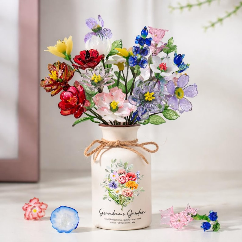 May include: A bouquet of colorful glass flowers in a cream-colored vase tied with twine. The vase is decorated with a floral design and the text "Grandma's Garden". Several loose glass flowers are scattered around the vase.