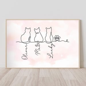 May include: A framed print featuring a minimalist line drawing of three cats and a paw print. The names "Oliver", "Max", and "Lucky" are written below the cats. The background has a soft pink watercolor effect.