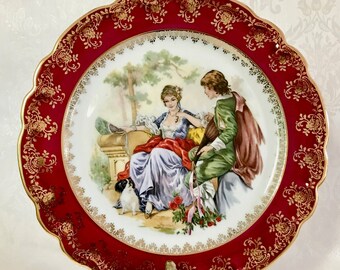 A beautiful Limoges Porcelain plate from the 1950s in red with a gold rim in excellent condition depicting 2 young lovers by JC Hunnick.