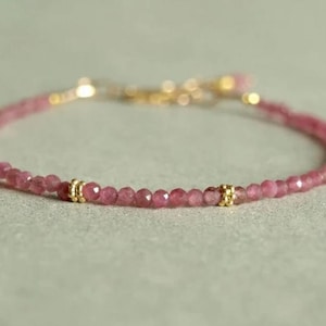 Pode incluir: Um delicado bracelete de pedras preciosas cor-de-rosa com detalhes dourados. O bracelete é feito de pequenas contas redondas e tem um design simples e elegante.
