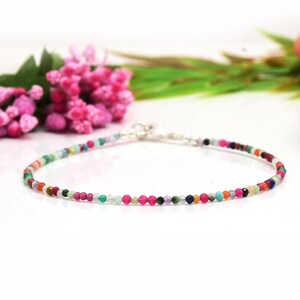 Puede incluir: Un delicado brazalete hecho con una variedad de cuentas de piedras preciosas de colores. El brazalete está enhebrado en una cadena de plata y tiene un cierre de plata.