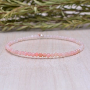 Könnte beinhalten: Ein zartes Armband aus rosa Opalperlen mit einem silbernen Verschluss. Das Armband besteht aus kleinen, runden Perlen, die auf einem dünnen Draht aufgereiht sind.