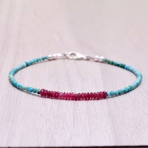 May include: A delicate bracelet featuring small, round turquoise beads and a central section of vibrant red ruby beads. The bracelet is secured with a silver clasp, creating a simple yet elegant design. The bracelet is approximately 7 inches in length.