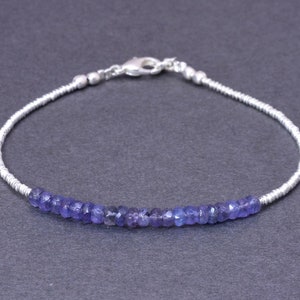 Puede incluir: Un brazalete de cadena de plata con una fila de pequeñas piedras preciosas de color azul claro. El brazalete tiene un cierre de langosta.