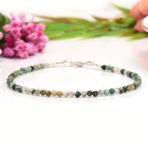 May include: A delicate bracelet made with green, brown, and white gemstone beads. The bracelet has a silver clasp.