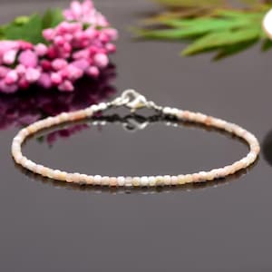 May include: A delicate bracelet made with small, pale pink opal beads. The bracelet has a silver clasp and is approximately 7 inches in length.