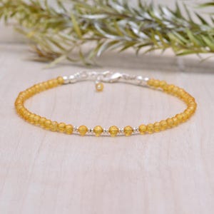 Puede incluir: Un brazalete delicado hecho con pequeñas cuentas redondas de ámbar translúcido y detalles plateados.