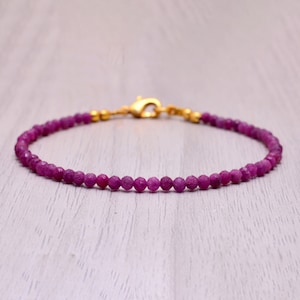 May include: A delicate bracelet made with small, round, pink gemstone beads. The bracelet has a gold clasp.