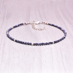 May include: A delicate silver chain bracelet with small, dark blue faceted beads. The bracelet has a lobster clasp closure.