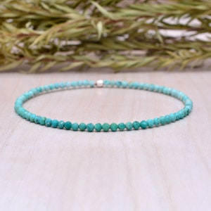 Op de afbeelding: Een delicate turquoise kralenarmband. De armband is gemaakt van kleine, ronde, turquoise kralen die aan elkaar zijn geregen met een zilveren sluiting. De armband wordt gepresenteerd op een lichtgekleurd houten oppervlak.