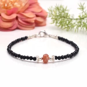 May include: A delicate bracelet with black onyx beads and a single sunstone bead. The bracelet is made with sterling silver beads and a lobster clasp.
