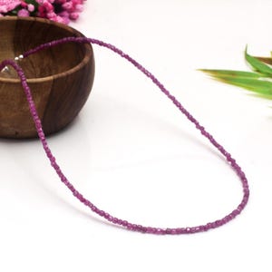 May include: A delicate necklace made with small, square-shaped pink ruby beads. The necklace is strung on a silver chain and is approximately 18 inches long.
