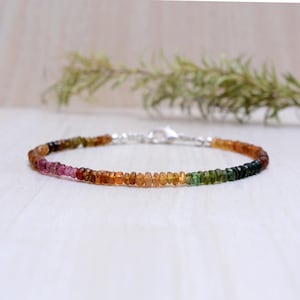 Pode incluir: Um delicado bracelete feito com pequenas pedras preciosas facetadas em tons de rosa, laranja, amarelo e verde. O bracelete é enfiado em uma corrente de prata com um fecho de lagosta.