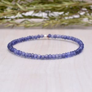 Può includere: Un braccialetto delicato realizzato con piccole perline di pietre preziose di colore blu chiaro sfaccettate. Il braccialetto è infilato su un filo d'argento.