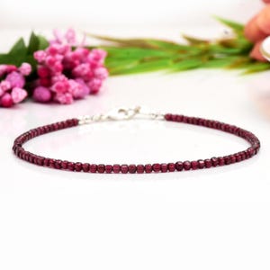 Puede incluir: Un delicado brazalete de plata con pequeñas cuentas de granate rojo oscuro. El brazalete tiene un diseño simple y un cierre de mosquetón.