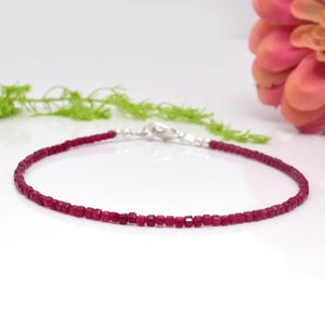 May include: A delicate bracelet made with small, square-shaped ruby beads. The bracelet is silver-toned and has a clasp closure.