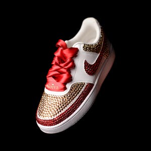 May include: White sneakers with red and gold rhinestones, red satin laces, and the word "Noiva" written on the side.