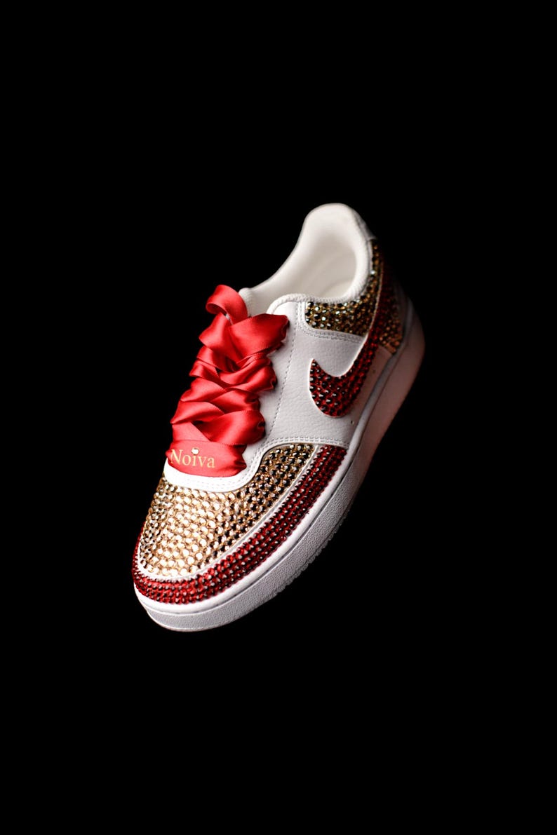 May include: White sneakers with red and gold rhinestones, red satin laces, and the word "Noiva" written on the side.