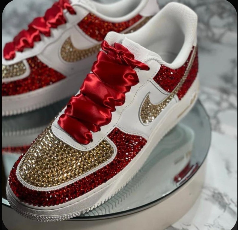 May include: White sneakers with red and gold rhinestones. The laces are red satin ribbon.