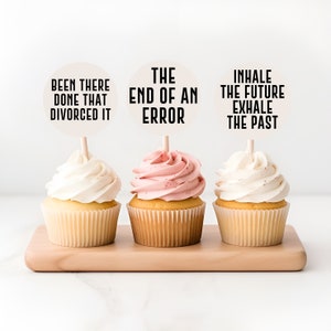 Peut inclure: Trois cupcakes avec un glaçage blanc et des décorations différentes. Les décorations sont rondes et blanches avec du texte noir. Le texte sur les décorations dit "Been there done that divorced it", "The end of an error", et "Inhale the future exhale the past".