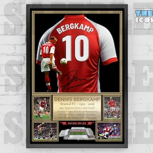 May include: A framed print of a red Arsenal football jersey with the name "BERGKAMP" and the number "10" on the back. The jersey is signed by Dennis Bergkamp. The print also includes photos of Bergkamp playing for Arsenal, including a photo of him scoring a goal. The print is titled "DENNIS BERGKAMP" and includes the text "Arsenal FC - 1995 - 2006" and "INVINCIBLES".
