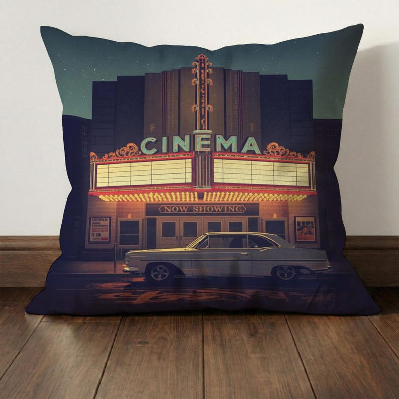 Może przedstawiać: Poduszka z motywem nocnego kina w stylu vintage. Na szyldzie widnieje napis "CINEMA" i "NOW SHOWING". Klasyczny samoch&oacute;d zaparkowany przed kinem. Tło jest granatowe z gwiaździstym niebem.