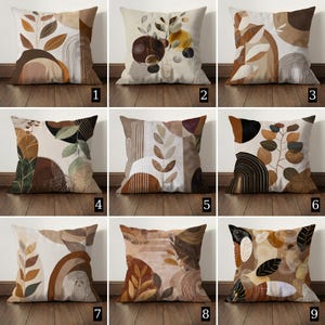 May include: Nine square throw pillows with abstract botanical designs in shades of brown, beige, and black. Each pillow features a unique pattern of leaves, arches, and geometric shapes. The pillows are displayed on a wooden floor.