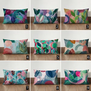 Può includere: Nove cuscini rettangolari con disegni botanici astratti in varie palette di colori. Ogni cuscino presenta un motivo unico di foglie, cerchi e forme organiche nelle tonalità di verde, rosa, blu e viola. I cuscini sono esposti su un pavimento in legno.