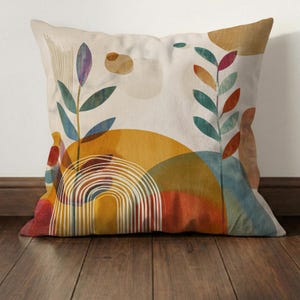 May include: Square decorative pillow with an abstract design. The pillow features a cream background with colorful shapes, including a yellow sun, a rainbow, and green and blue leaves. The pillow is placed on a wooden floor.