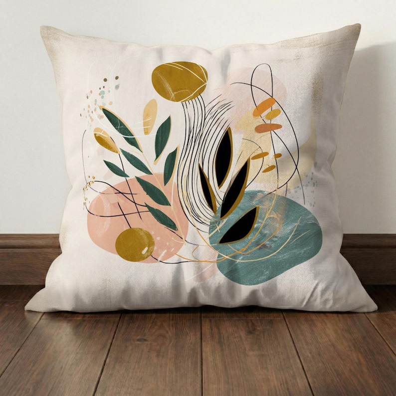 May include: Square throw pillow with an abstract design. The pillow features a cream-colored background with a colorful, artistic design. The design includes black, green, gold, pink, and teal shapes and lines, creating a modern aesthetic.