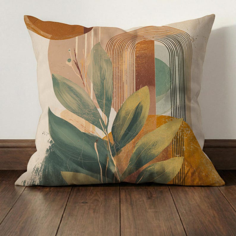 May include: Square decorative pillow with an abstract botanical design. The pillow features large green leaves, geometric shapes in shades of brown, yellow, and green, and a beige background. The pillow is placed on a wooden surface.