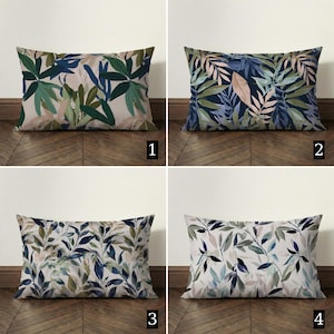 May include: Four rectangular cushions with botanical leaf patterns. The cushions feature various colour schemes, including green, blue, and beige leaves on a light background. The cushions are arranged on a wooden floor.