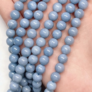 May include: Close-up of strands of light blue, round gemstone beads. The beads are smooth and have a slightly glossy finish. The beads are strung together, suitable for jewellery making or other craft projects.