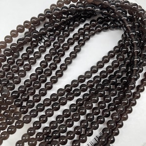 May include: A strand of dark brown gemstone beads. The beads are round and smooth, and they are strung on a clear thread. The beads are approximately 6mm in diameter.
