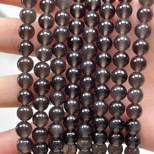 May include: A strand of dark gray agate beads with a speckled, translucent finish. The beads are round and smooth, and they are strung on a clear elastic cord.