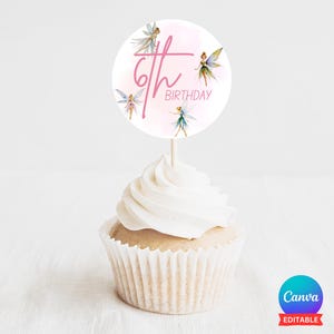 以下が含まれることがあります： ピンクと白のカップケーキの飾り。ピンクの背景に「6th Birthday」の文字と妖精のイラストが描かれています。