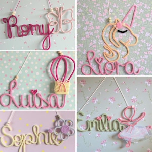May include: A collection of five wall-hanging name signs crafted from knitted yarn cord. Each sign features a custom name in cursive script paired with a decorative shape, including a butterfly, unicorn, hot air balloon, flower, and ballerina.